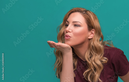 An attractive girl sends a kiss or blows on the hand. Blonde posing on blue background.