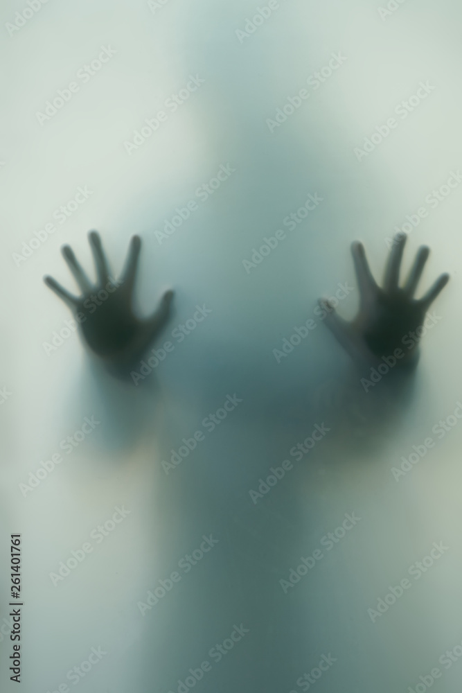 Ghostly silhouette of a girl with outstretched hands, fingers outstretched behind the translucent glass doorBlurred shadow of a horror woman. The hands on the glass.