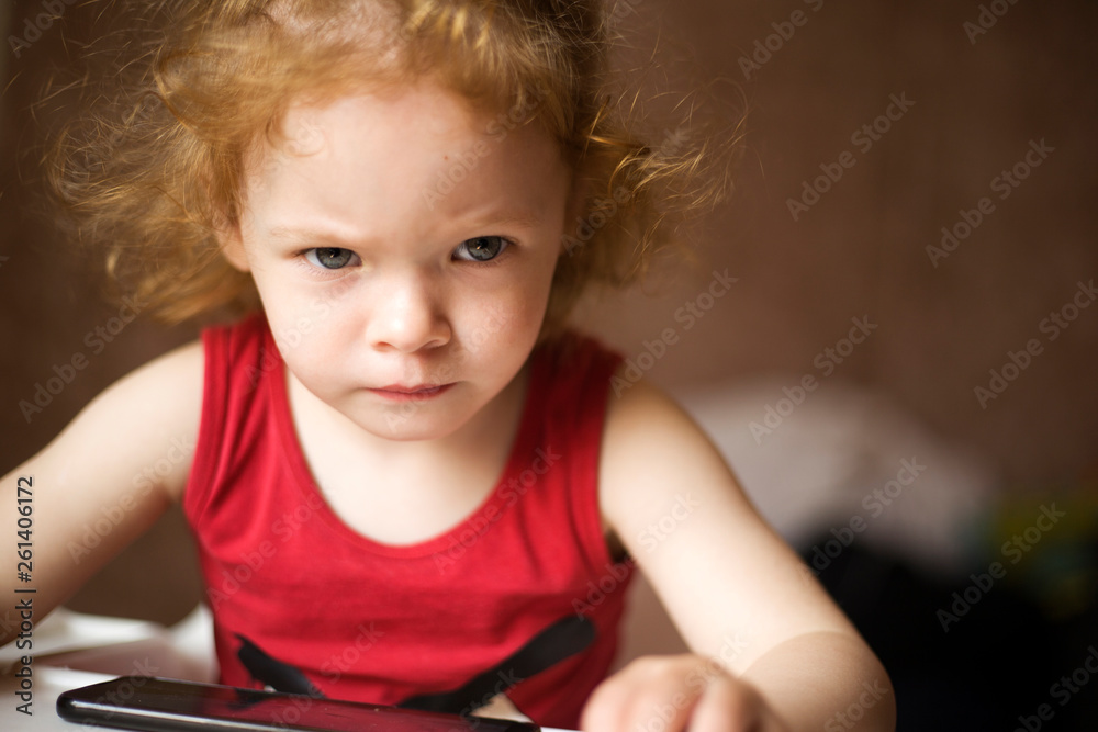 Φωτογραφία the little red-haired girl is watching cartoons on the phone , a beautiful baby
