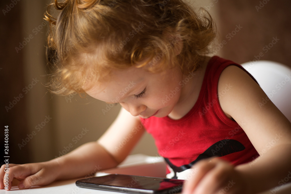 Φωτογραφία the little red-haired girl is watching cartoons on the phone , a beautiful baby