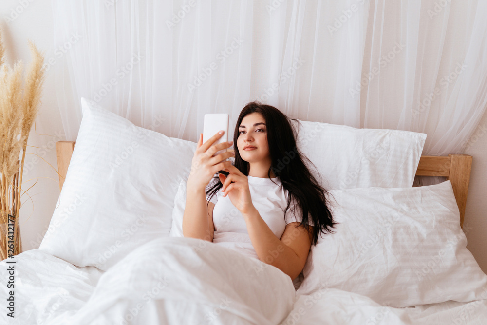 Relaxed woman using a smart phone at home bed. Mobile app, device addiction, internet browsing and leisure Relaxed woman using a smart phone at home bed. Mobile app, device addiction, internet browsing and leisure