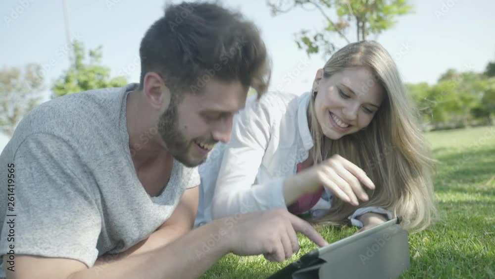 Medium shot of smiling young couple using digital tablet while lying in park Medium shot of smiling young couple using digital tablet while lying in park