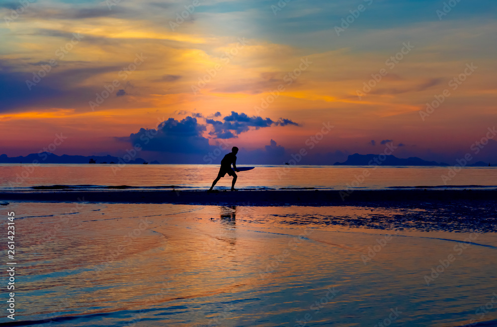 Silhouette of man with surfboard on the beach with twilight sky background