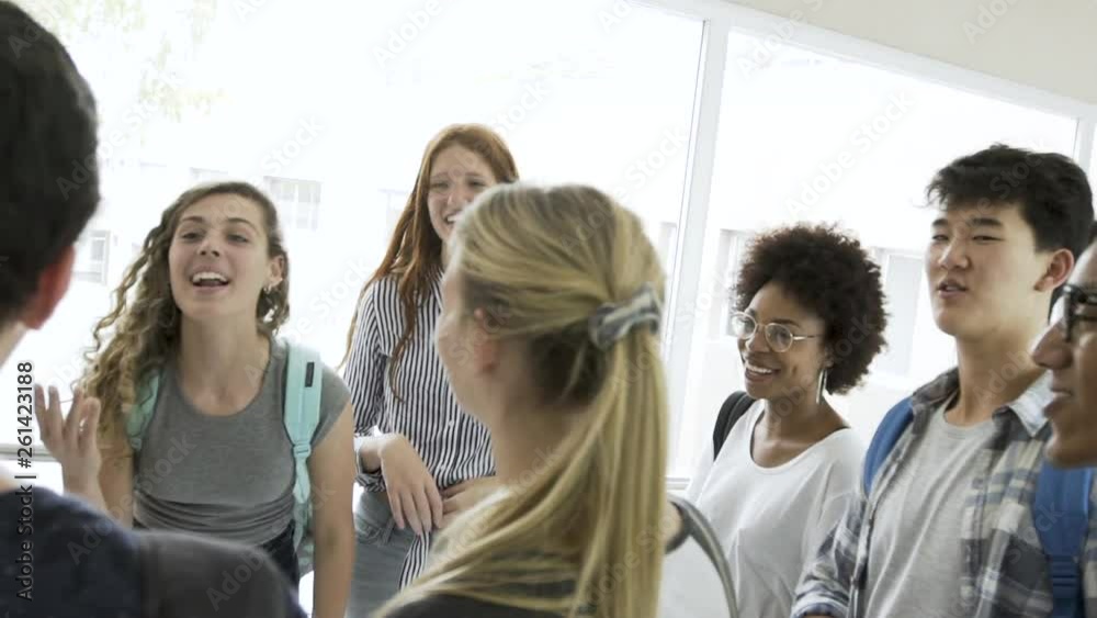 Panning shot of college students talking with each other while standing in corridor Panning shot of college students talking with each other while standing in corridor