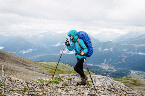 Girl tourist with a backpack climbs the mountain in bad weather. The concept of overcoming obstacles and achieving the goal in the hike.