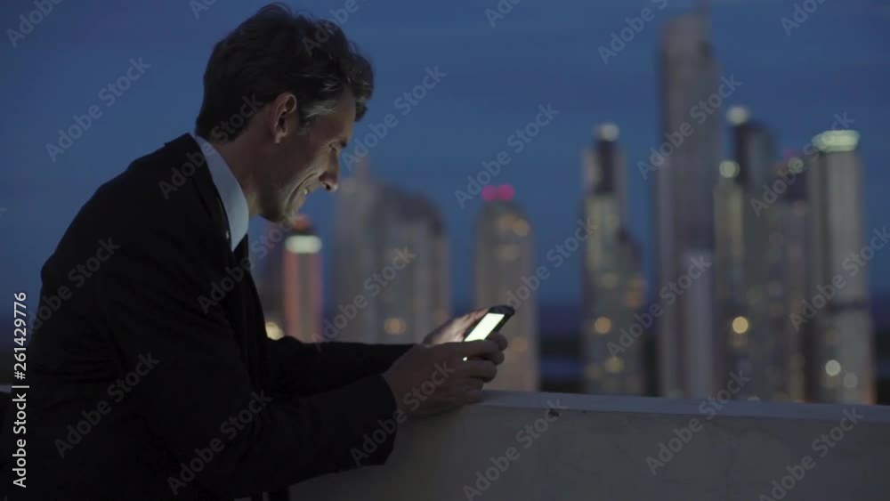Medium shot of mature businessman text messaging on smartphone while standing on terrace Medium shot of mature businessman text messaging on smartphone while standing on terrace