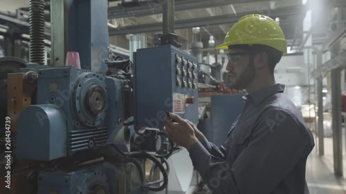 Medium shot of engineer using smart phone and examining machinery in factory