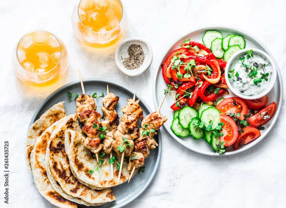 Summer lunch table - turkey skewers, tortillas, tomatoes, cucumber salad, baked sweet pepper, yogurt herb sauce and summer fruit cocktail on a light background, top view Summer lunch table - turkey skewers, tortillas, tomatoes, cucumber salad, baked sweet pepper, yogurt herb sauce and summer fruit cocktail on a light background, top view