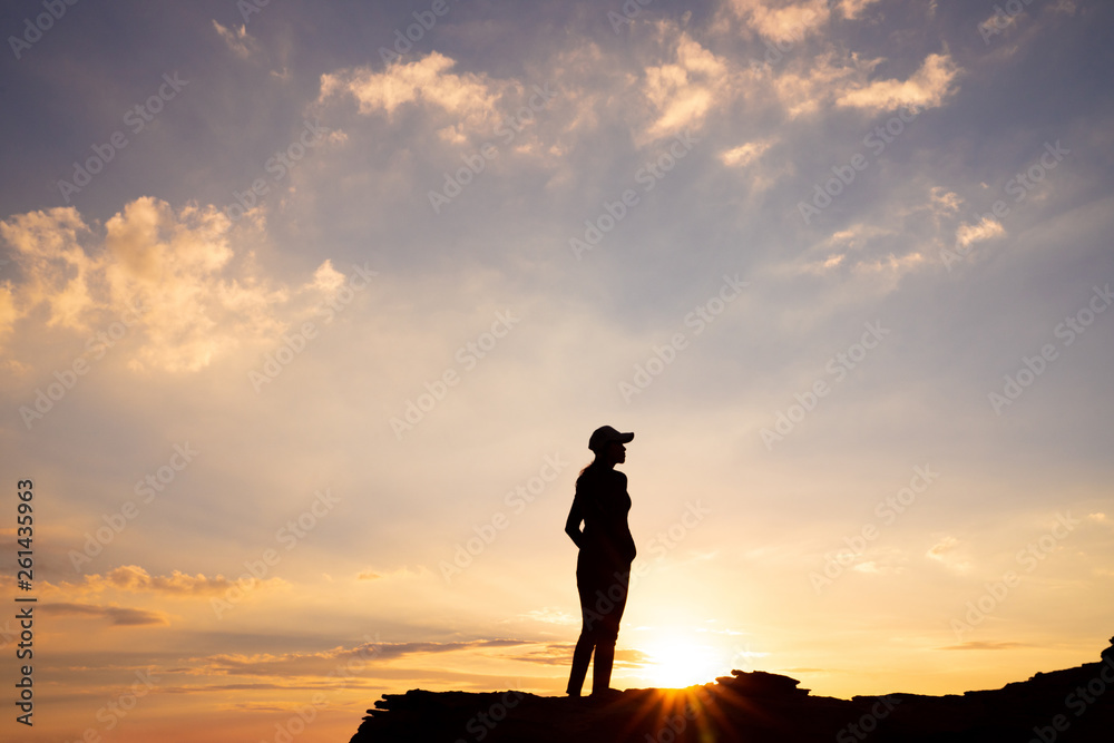 A silhouette of a woman standing on top of a cliff with sunset sky background in Wadi Rum desert, Jordan.