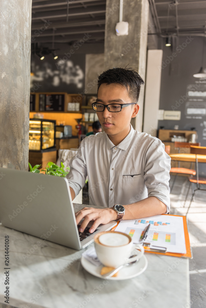 Fototapeta premium Young Asian freelancer working on laptop at cafe