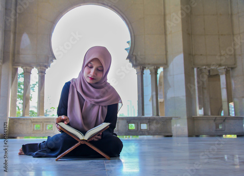 Young malay muslim woman reading the holy Quran in a mosques.