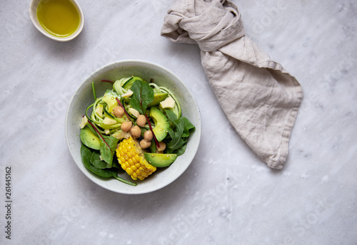 fresh vegan salad bowl with avocado, spinach, corn, chickpeas, zucchini on marble background with copy space