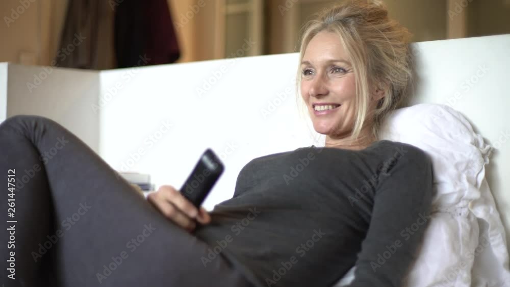 Medium shot of a medium shot of a mature woman watching TV while relaxing on a bed Medium shot of a medium shot of a mature woman watching TV while relaxing on a bed