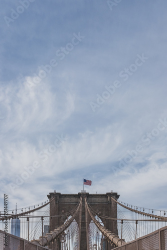 US flag flying over Brooklyn Bridge, under sky and clouds, in New York, USA