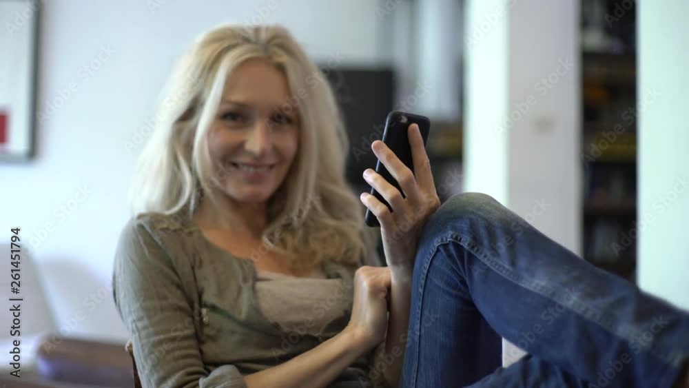 Medium shot of a smiling mature woman texting on her smart phone while sitting on the chair at home
