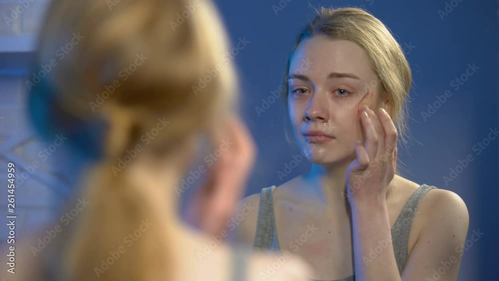 Terrified young woman covering face wound with concealer front of home mirror Terrified young woman covering face wound with concealer front of home mirror