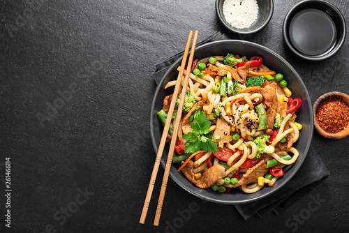Photo Udon stir fry noodles with pork meat and vegetables in a dark plate on black stone background