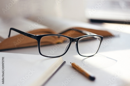 On a light background and a table among the books are glasses in a black elegant frame