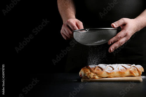 man powder of sugar to pie on dark background. decorating dessert concept with ingredients