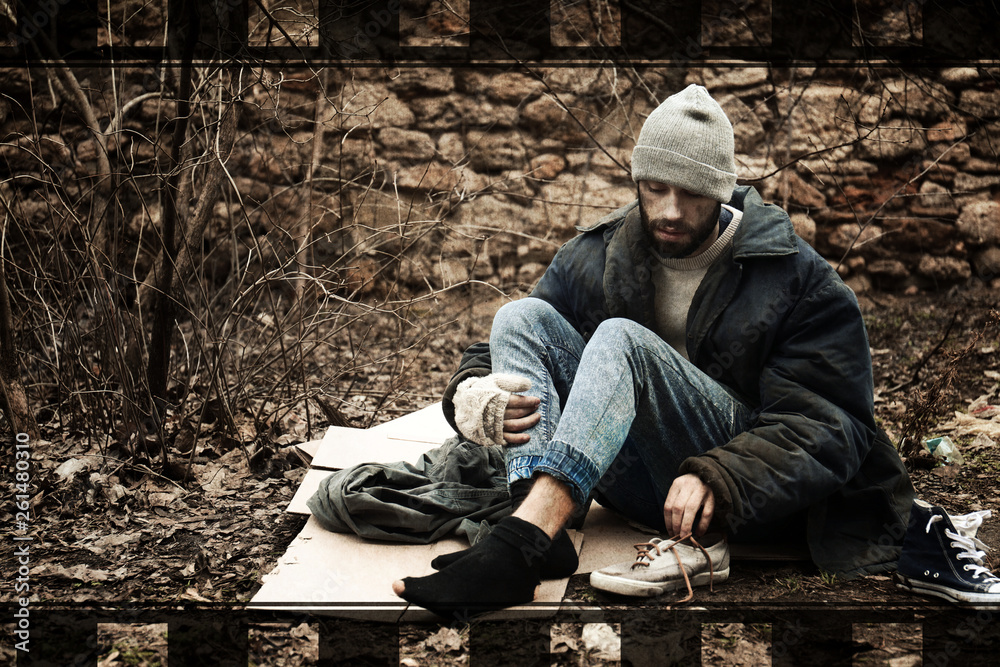 Poor homeless man sitting on cardboard in city park