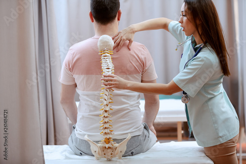 Photography Young attractive female doctor holding spine model and truing to realize where is patient's painful place