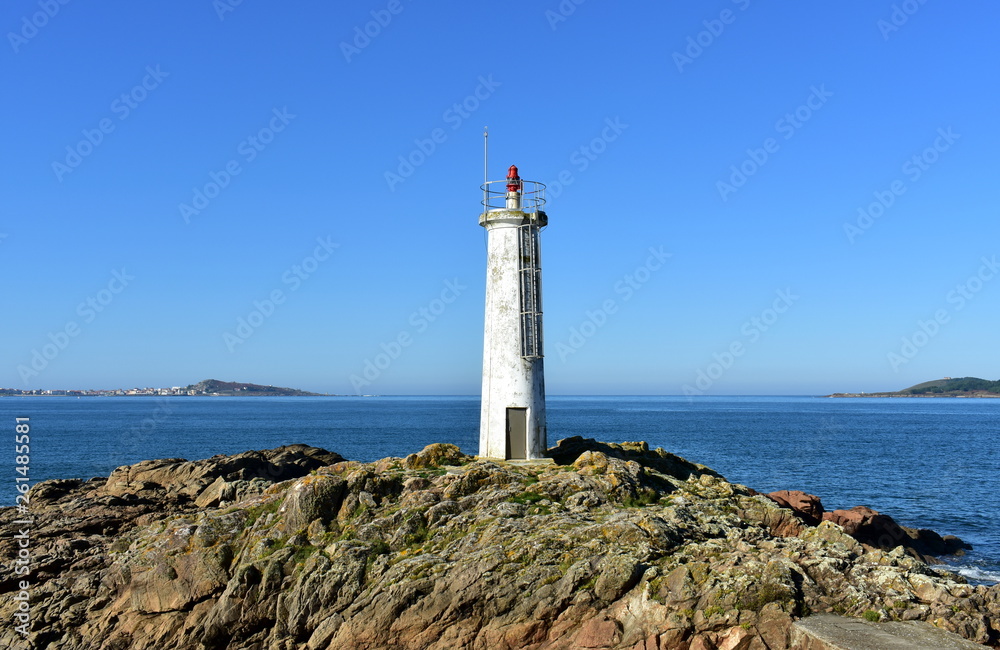 Old white lighthouse on the rocks with blue sea and sunny day. Galicia, Spain.