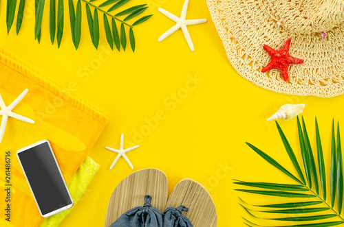 Top view summer beach accessories. Frame banner with tropical palm leaf branches, towel and beach slippers on yellow background with space for text. Summer flat lay background