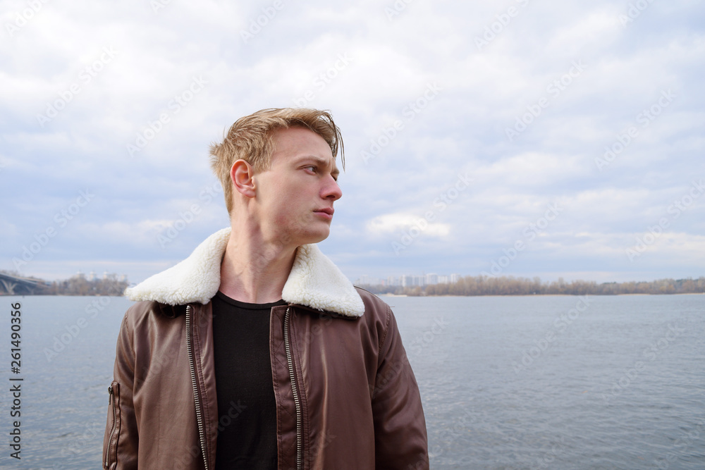 Young blond guy in a leather jacket near the river. Young blond guy in a leather jacket near the river.