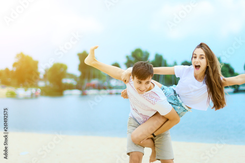 Young couple in love female girl and male man teenagers adults having fun and enjoying weekends near water, river, lake at hot sunny summer day at sand beach. Summer hobbies leisure activities concept