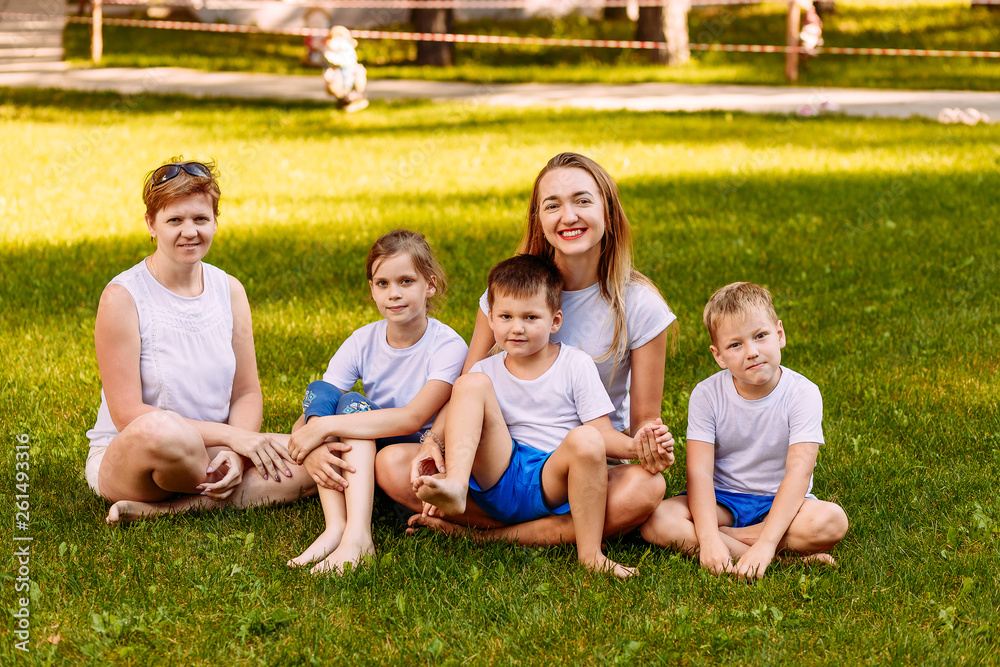 two women and three children sit on green grass two women and three children sit on green grass