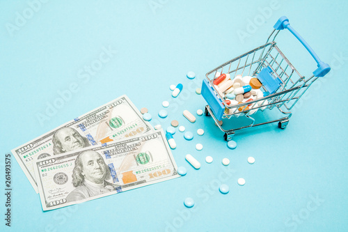 Dollars, pills and shopping cart on a blue background. Pharmacy concept. Copy space