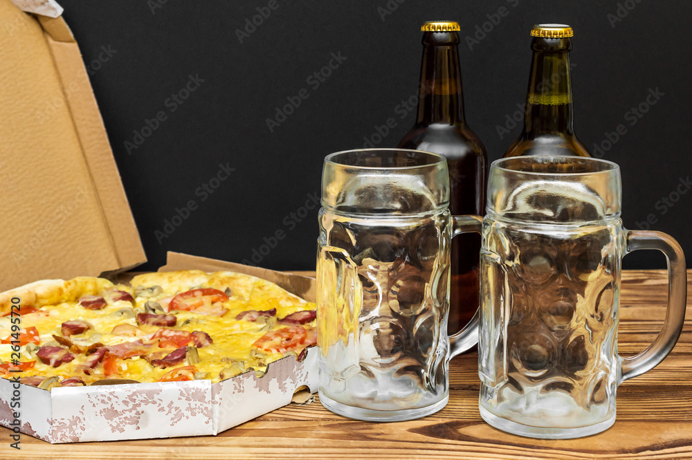 Pizza in pizza box with bottles of beer and beer glasses on the table. Pizza in pizza box with bottles of beer and beer glasses on the table.
