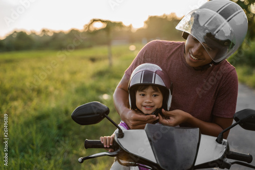 daddy help her daughter to fasten the helmet while riding a motorcycle scooter © Odua Images