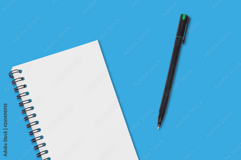 One paper notepad with spiral binder and blank sheets near black plastic pen lies of blue office table. Top view. Copy space for your text. Concept of business or education One paper notepad with spiral binder and blank sheets near black plastic pen lies of blue office table. Top view. Copy space for your text. Concept of business or education