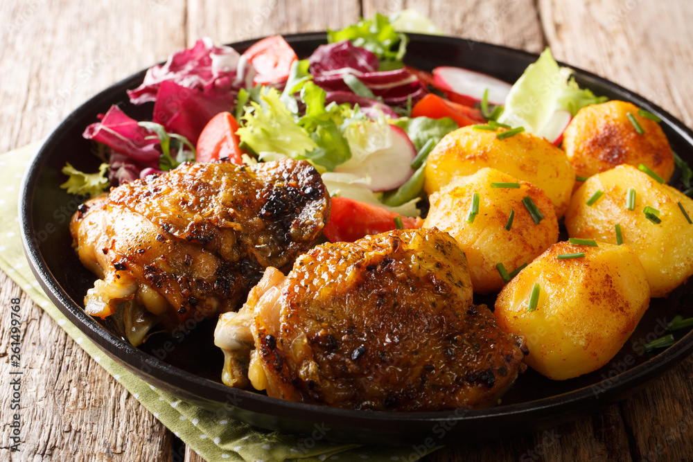 Baked chicken thighs with a garnish of new potatoes and fresh salad close-up on a plate. horizontal