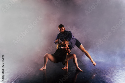 Fototapeta Naklejka Na Ścianę i Meble -  Two modern dancers stretching their shoeless feet high in the air surrounded by smoke on stage.