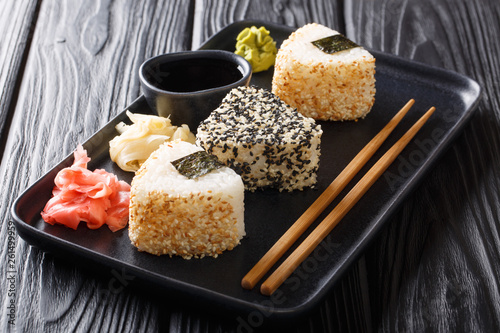 Triangular onigiri with sesame served with ginger, wasabi and soy sauce close-up on a plate. horizontal photo