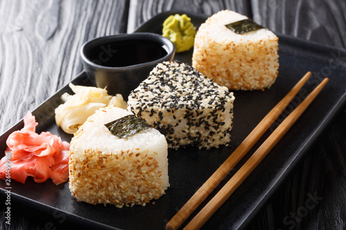 Portion of onigiri triangular rolls in sesame served with ginger, wasabi and sauce close-up on a plate. horizontal