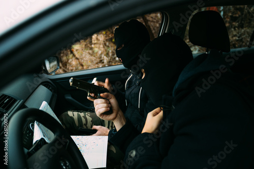Bank robbers with their masks on pointing at the map prepared for robbing the bank,sitting in the car and waiting for the right time to rob. © qunica.com