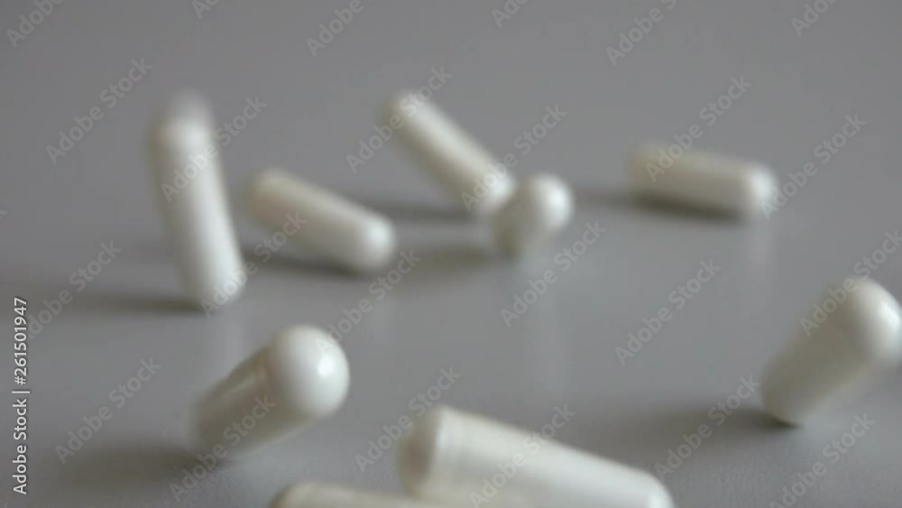 Tablets on a gray background. Pills. Medicine and healthy. Close up of capsules. Many white medical capsules falling down on the gray table. Slow motion. Closeup.
