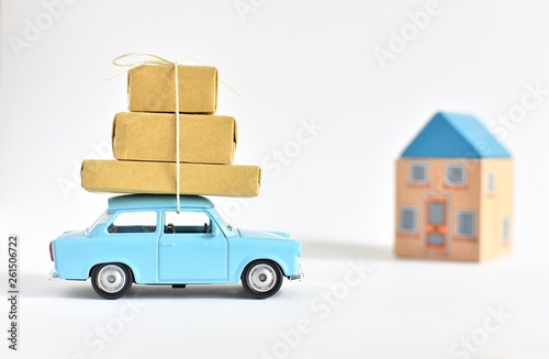 Moving in concept, blue toy car with brown boxes on the roof, new house behind. © IndrePau