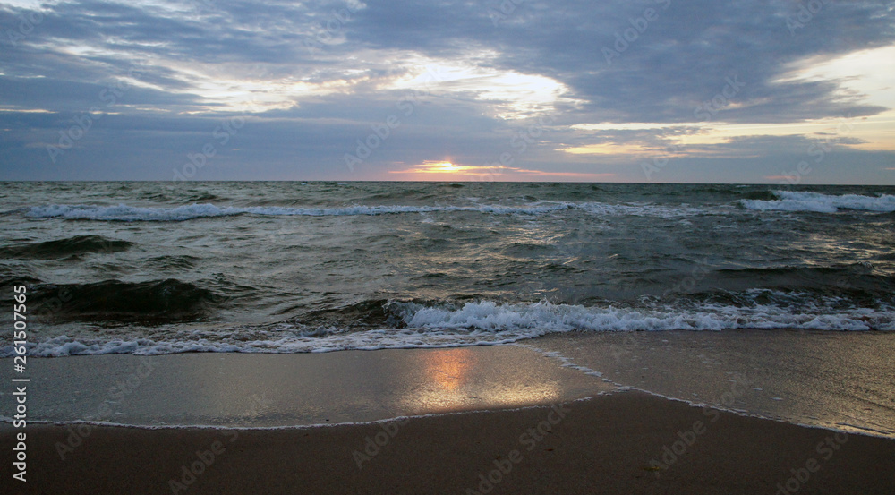 Summer evening sunny sunset in the sea on the shore. Sandy coast on the ocean.