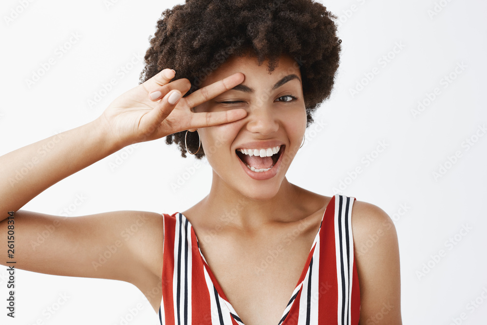 Pure joy and happiness. Portrait of satisfied happy and feminine dark-skinned woman feeling amused and excited, greeting best friends, winking and smiling broadly, showing victory sign over eye