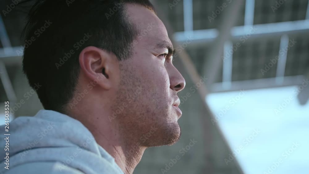 Close portrait of urban serious man, looks into the distance, standing under the modern solar panel, in urban landscape, dressed in grey hoodie on sunset light, waiting for a friend, Close portrait of urban serious man, looks into the distance, standing under the modern solar panel, in urban landscape, dressed in grey hoodie on sunset light, waiting for a friend,