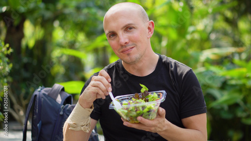 Happy Smiling Young Man Eating Healthy Salad While Looking Into Camera