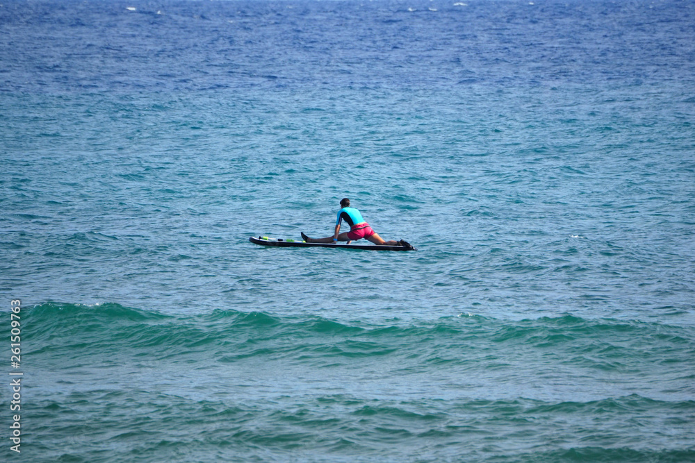 girl sits on a splits in the ocean on paddleboard. back view.