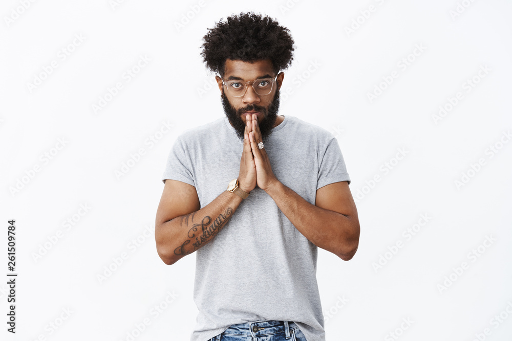 Student bowing to sensei. Portrait of devoted and serious-looking calm african american adult bearded guy in glasses with tattoos and piercing nodding making namaste greeting with hands together Student bowing to sensei. Portrait of devoted and serious-looking calm african american adult bearded guy in glasses with tattoos and piercing nodding making namaste greeting with hands together