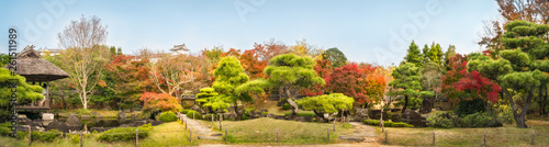 Chinese style garden panorama in autumn at Koko-en Japanese Gardens with small stone bridges over the creek and with the rooftop of Himeji Castle in the background  in Japan.