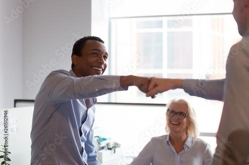 Two excited diverse male workers give fist bump celebrate teamwork