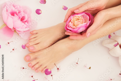 Woman is taking bath. Close up of female feet and hands in bath full of water and flowers.